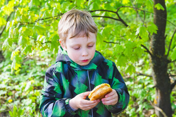 The boy is surprised by a delicious doughnut. A child holds a sweet treat in the Park in his hands. The kid was going to eat a doughnut with frosting.