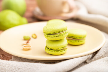 Green macarons or macaroons cakes with cup of coffee on a brown concrete background. Side view, selective focus.