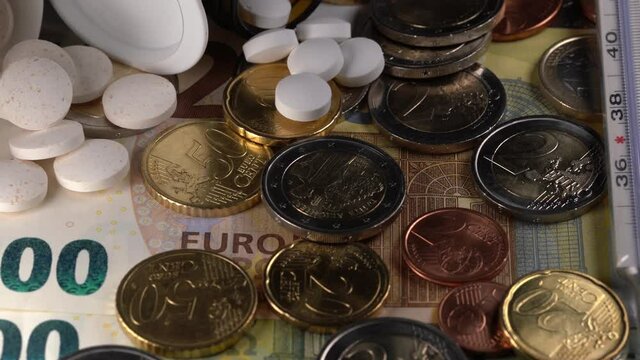 pills and medicine on top of Euro coins and banknotes with fever thermometer