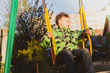 A teenage boy in a green jacket is thoughtful. A child swings on a swing.