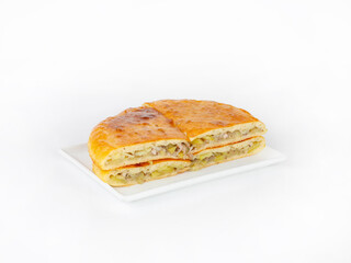 Pie with meat and potatoes cut in half lies on a plate on a white background