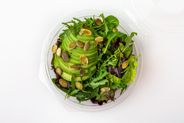 Salad in plastic package for take away or food delivery isolated on a white background. Nutritional Diet Snack with avocado, herbs, pumpkin seeds.