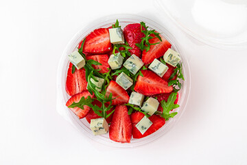 Salad in plastic package for take away or food delivery isolated on a white background. Nutritional Diet Snack with strawberries, dorblu cheese and arugula.