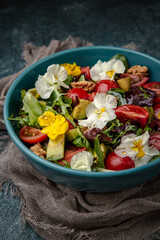 Diet vegetarian salad of cherry tomatoes, avocado, mix of greens with flowers.
