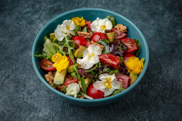 Diet vegetarian salad of cherry tomatoes, avocado, mix of greens with flowers.