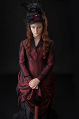 A young Victorian woman in a dark red and black ensemble against a black backdrop