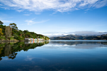 Fototapeta na wymiar Colorful Boat Sheds with beautiful reflection on daytime at Duvauchelle, Akaroa Harbour on Banks Peninsula in South Island, New Zealand.