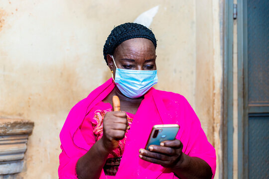 elderly black african senior woman wearing face mask using her mobile phone checking and researching about corona virus