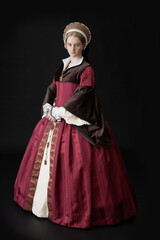 A young woman in a red Tudor dress against a black bacdrop - obrazy, fototapety, plakaty