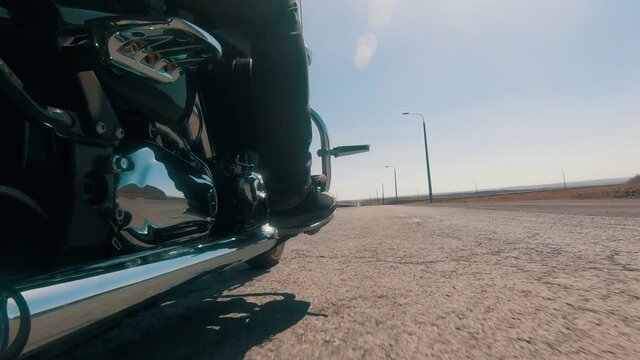 a motorcyclist rides a motochopper on a vacant lot, on a straight road. Reflection of hills on the exhaust pipe, close-up