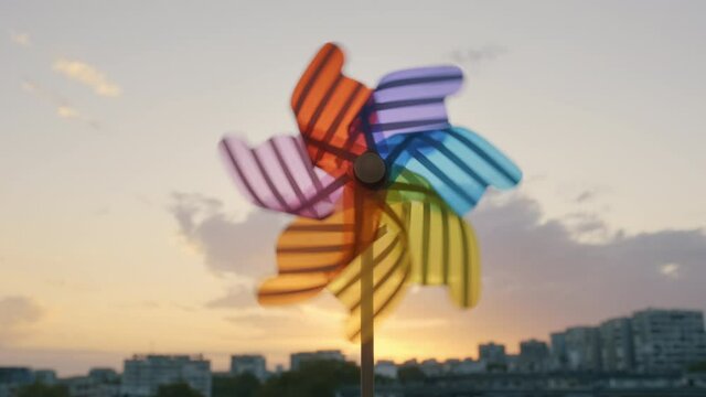 Pinwheel rotating colored plastic with blowing wind against a blue sky, white clouds, silhouettes of city buildings on sunset slow motion. Symbol of freedom and life. Toy spinner. Bright disk of sun