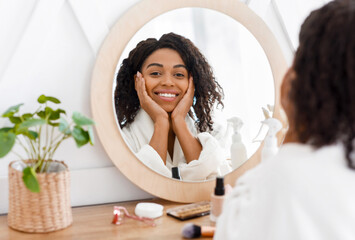 Beautiful Black Woman In Bathrobe Sitting At Dresser Table, Looking To Mirror