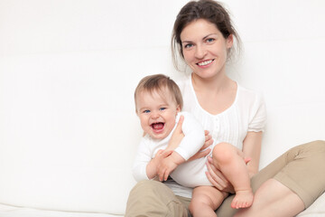 Happy mother playing with baby on white sofa