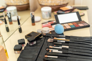 Desktop of a professional makeup artist with a variety of cosmetics on it. Brushes are laid out in a black leather case, shadow palettes, sponge, jars of cosmetics.