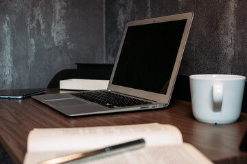 Fototapeta premium Modern wooden workplace with a notebook, tea, pen, diary and a mobile phone. Grey wall