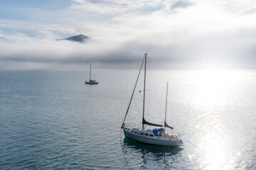 Fototapeta premium Blue sky, white clouds, mist & aquamarine seas at Akaroa Harbor. Anchored are fishing boats & sailboats, along the Port at Akaroa, Canterbury, New Zealand.