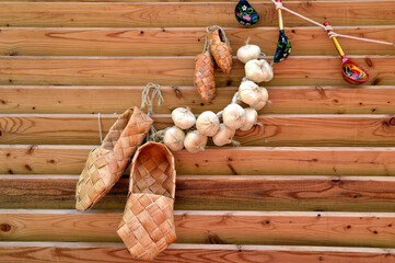 Russian traditional ancient bast shoes with bunch of garlic and rope with hunging wooden spoons. Composition in Russian Slavic style. 