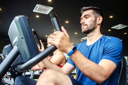 Portrait of young man exercising using stationary bike in gym with a group of people. Fitness class doing sport biking in the gym for health