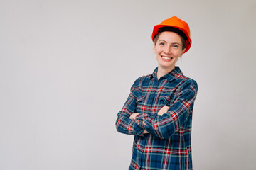 Portrait of a young smiling girl builder in a plaid shirt in an orange protective helmet against a light background
