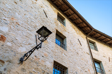Fototapeta na wymiar Lampada per illuminazione pubblica e finestre su muro di sasso in edificio storico del borgo medievale di Strassoldo.