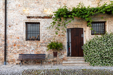 Fototapeta na wymiar Porta d'ingresso con finestre e panca. Bellissima facciata di casa storica in centro medievale di Strassoldo.