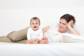 Happy mother playing with baby on white sofa