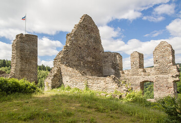 The ruins of a medieval castle, illuminated by the sun on a slightly cloudy summer day.