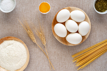 Raw eggs, white flour, whole wheat pasta on cotton fabric background.