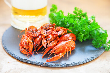 Boiled red crayfishes with a beer and green vegetableson a ceramic board. Close up. Selective focus.