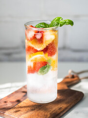 Fresh Summer Homemade lemonade with orange slices, strawbereies, basil and ice in glass on a white table.