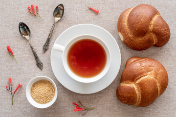 Top view of Fresh Bread Rolls, cup of tea, dark sugar, vintage spoons, red flowers on cotton fabric background. Top view. Breakfast, Morning concept.