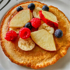 Top view of a vegan pancake served with various delicious and colorful fruits.
