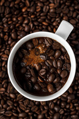 coffee in a white cup on a background of coffee beans, coffee grains and cinnamon stick in coffee foam
