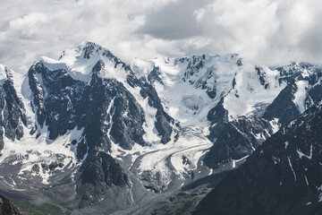 Obraz premium Atmospheric alpine landscape with massive hanging glacier on giant mountain. Big glacier tongue on mountainside. Low clouds among snowbound mountains. Cracks on ice. Majestic scenery on high altitude.