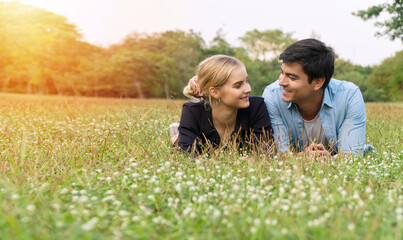 Fototapeta premium Joyful young couple looking each other lying together on the green grass in summer sunny park feeling relaxation. Lifestyle and relationship concept.