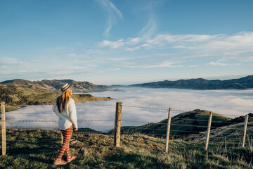 Happy carefree asian woman enjoying nature with layers of mountains and the mist in the morning at The peak of Bank Peninsula, Akaroa, New Zealand.