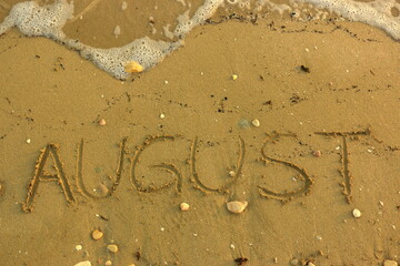 August Hand Written on Sandy Texture at a Sunny Beach with Pebbles with Sea Water in the Background. Travel in the Summer Months Tourism Wallpaper Image. Seascape Vacation Concept.