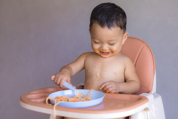 Asian boy eatting on high baby chair.