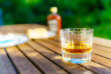 Sommerstimmung im Garten mit Whiskeyglas, Glas, Gartentisch in abendlichem Sommerlicht