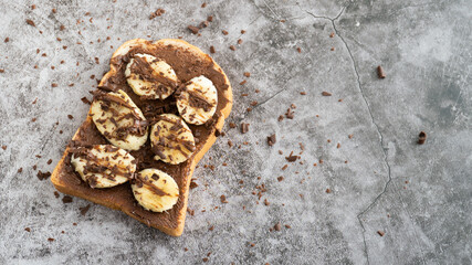 A single slice of toast bread with chocolate spread and chocolate curls shavings top on slice bananas.