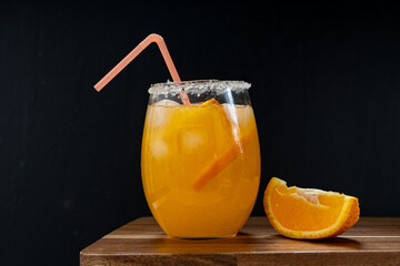 Fresh cold orange juice cocktail with ice cubes and orange slices on wooden bar counter
