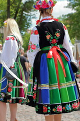 oung woman wears a traditional embroidered folk dress from Lowicz region Poland (Lowicz is name of city in central Poland) , back, in the background another woman dressed in folk dress, Corpsu Christi