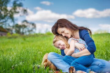 Fototapeta premium Mother and daughter sitting on summer meadow with green grass