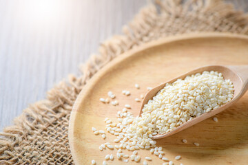 White sesame seeds in a wooden spoon on wood table.