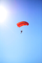 A man parachutes to the ground against a blue Sunny sky. The sun shines on the skydiver, skydiving landing with a parachute.