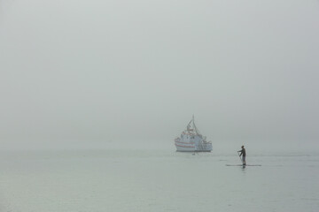 Stand Up Paddle or SUP board surf in the fog at Akaroa harbor, Akaroa, New Zealand.