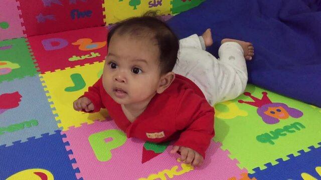 Cute baby learn how to crawl. Funny baby laying with flying pose on a puzzle floor. 5 months old baby development milestone. Stay home baby.