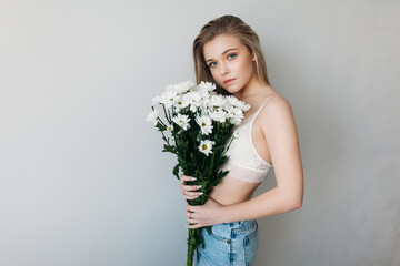 A beautiful girl with a covered face with light hair in her underwear holds a bouquet of daisies. A festive bouquet of daisies in the focus of the lens. A gift for women's day or mother's Day.