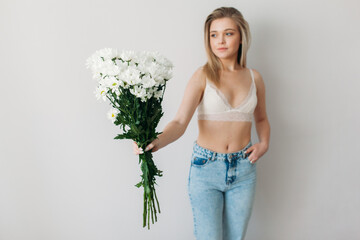 A beautiful girl with a covered face with light hair in her underwear holds a bouquet of daisies. A festive bouquet of daisies in the focus of the lens. A gift for women's day or mother's Day.