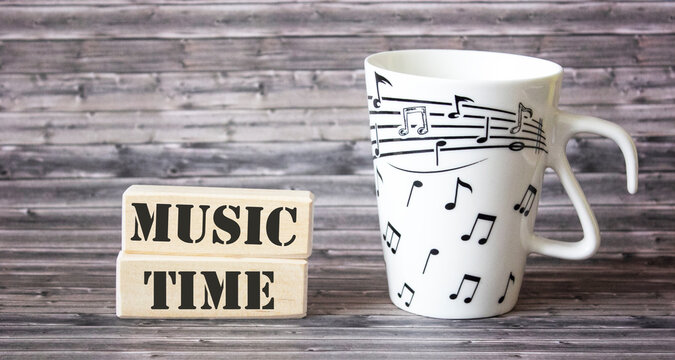On a wooden table are blocks with the text music time and a mug with notes on it.